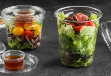 How Food Brands Should Choose Disposable Plastic Food Containers Clear cups with layered salad greens, cherry tomatoes, and peppers; dressing served in a separate small cup beside them (takeaway salads).