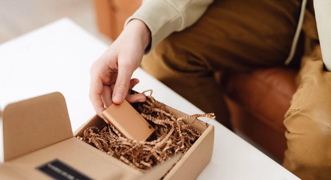 Hand is unwrapping a chocolate bar from a gift box filled with crinkle paper.