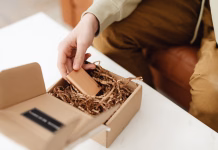 How To Package Your Business’s Promotional Gifts For Maximum Impact Hand is unwrapping a chocolate bar from a gift box filled with crinkle paper.