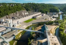 Norske Skog Approves PM6 Rebuild to Expand Kraftliner Production Aerial view of a large industrial quarry with long buildings, conveyors, and piles of material beside a winding river and green hills.